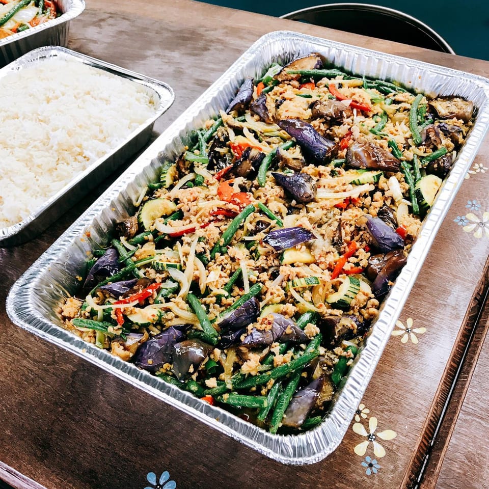 Asian stir-fry with eggplant, green beans, and ground meat in a foil tray next to white rice.